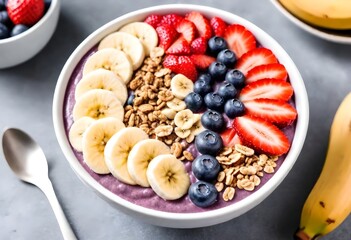 A bowl of acai berry smoothie bowl topped with sliced bananas, strawberries, blueberries, and granola