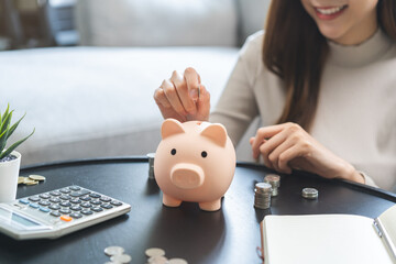 Saving money wealth concept, asian young business woman hand putting coin into piggy for saving...