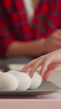 Little child hand reaches to eggs while elder sister prepares Ebru decor in living room closeup slow motion. Unusual Easter holiday decoration