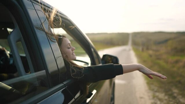 free girl hand out of the window rides a sunset car wind in the face. concept car travel on the road. girl stretches her hand out of the car sun window glare. movement driver hand out of the window
