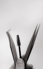 A hand holds two tweezers and a brush for eyelash extensions.