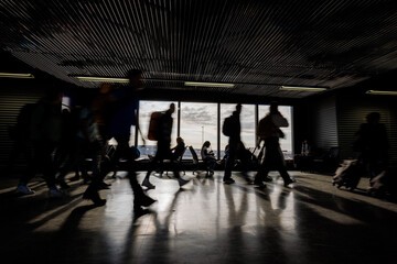 Passengers with luggage walking along an empty airport departure lounge, handheld motion blur shot. Traveling lifestyle concept.