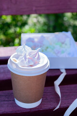 A glass of coffee on a wooden background and meringue in a box against a background of nature.