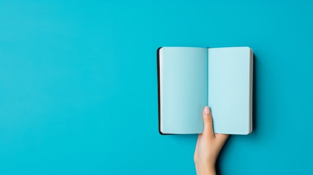 Creative theme captured in an advertising photo of a hand holding a notebook, vibrant blue background, inspiring imagination and ideas