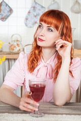 Beautiful young redhaired woman with glass of wine sitting in the kitchen
