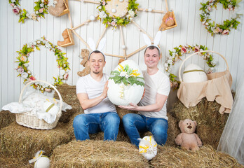 Two man with rabbit ears sitting on the haystack and holding Easter egg