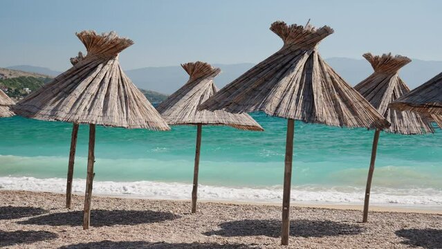 Straw umbrellas on Vela beach in Baska in Croatia on the island of Krk. The turquoise Adriatic Sea and waves crashing on the shore.