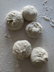 Five dough balls on the countertop with flour ready to bake