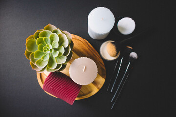Candles, wooden board, makeup brushes, powder and cactus on a black background. Copy space