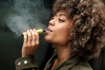 Side view of curly woman smoking an e-cigarette.