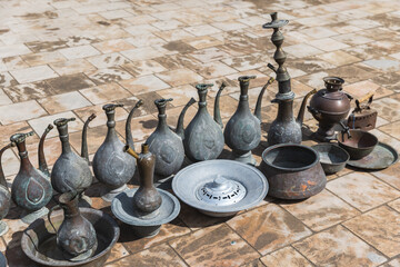 Ancient jugs and other dishes for sale stand on the pavement - obrazy, fototapety, plakaty