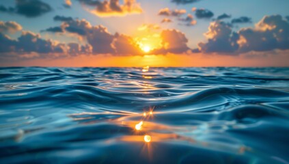 The sun is setting over the ocean, casting a warm glow on the water. The sky is filled with clouds, creating a serene and peaceful atmosphere. The water is calm and still