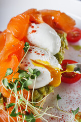 poached egg toast with avocado and salmon on a white plate