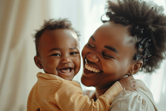 Loving mother hugs a little baby at home. Pretty woman holding cuddling newborn child in her arms, laughing with him. Happy family smiling together. African mom carrying kissing small infant on hands.