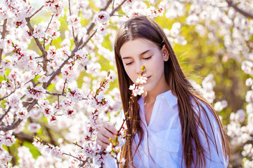 Pretty teen girl are posing in garden near blossom cherry tree with white flowers