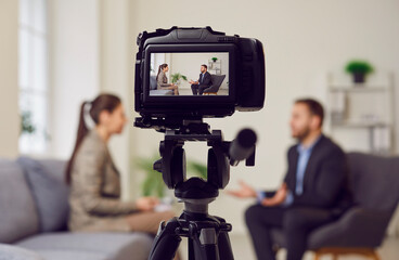 Camera on tripod foreground, businessman giving interview to journalist in office, female reporter...