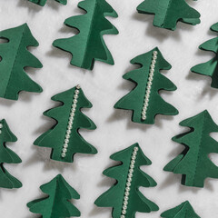 Christmas craft background with handmade Green xmas trees cut of paper on white fur, firs decorated pearls. DIY eco friendly sustainable christmas decoration, top view minimal aesthetic pattern