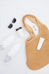 Straw bag for beach, glass of coffee, tube of lotion, sunglasses on white background. Summer and beach accessories.