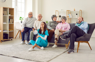 Group of happy diverse senior people sitting on sofa together watching TV in retirement home with a...