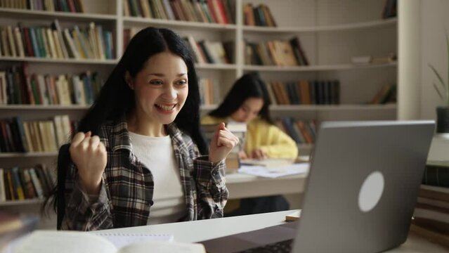 Pretty young woman student with crossed fingers wait for news celebrate exam result online win success reading great news feel amazed happy reading message email on laptop at university library
