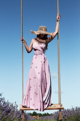 Young sexy beautiful woman swinging on hanging vintage swing in a lavender field against the background of the sky.	 - obrazy, fototapety, plakaty