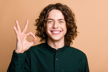 Photo of positive satisfied nice man dressed green trendy clothes showing gesture okey symbol isolated on beige color background