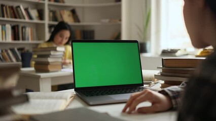 Over-the-shoulder view of student looking at laptop green screen chroma key template mock up for design advertising at university library