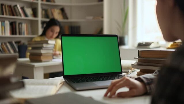 Over-the-shoulder view of student looking at laptop green screen chroma key template mock up for design advertising at university library