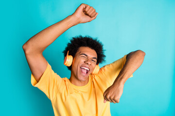 Portrait of crazy eccentric man with afro hairstyle wear oversize t-shirt enjoy rock music in headphones isolated on teal color background