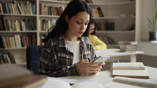 Smiling young woman hold smartphone scrolling social media online while take a break at university library Pretty student relax enjoying great day after lessons indoors 