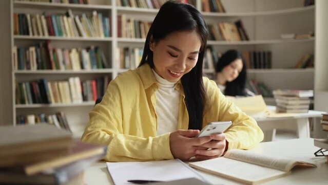 Smiling young asian woman hold smartphone scrolling social media online while take a break at university library Pretty student relax enjoying great day after lessons indoors 