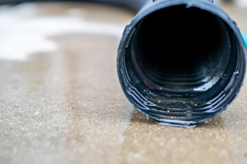 Selective focus on the front opening of a residential sump pump discharging water from the end of a flexible black hose