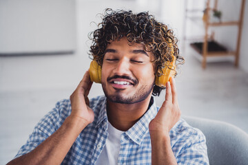 Photo of handsome dreamy guy dressed plaid shirt enjoying music headphones indoors room home house