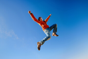 Obraz premium Energetic young man leaping high against a clear blue sky
