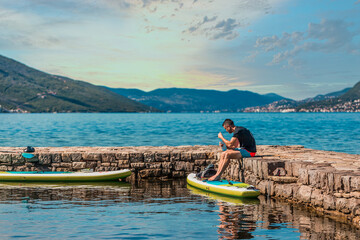 young adventurer standing by a calm lake with paddleboard ready for a day of water activities surrounded by mountains