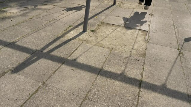 On the ground are the shadows of children swinging on a swing on a playground in a city park on a hot sunny day.