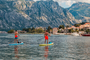man enjoying stand-up paddleboarding on serene blue waters with a picturesque coastal town backdrop...