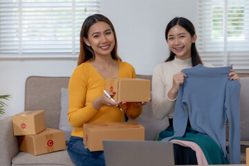 Two smiling women packing clothing items for online shop orders, sharing a joyful moment.