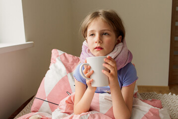 sick little girl lying on bed at her home, drinking hot tea, looking into the camera, sick child