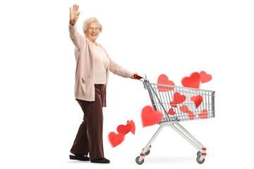 Full length shot of a senior lady waving and pushing a shopping cart with hearts