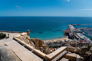 Santa Barbara Castle (Costa Blanca, Alicante, Spain). View of the defensive walls (castle ruins) and the city beach (Playa del Postiguet). Typical Spanish holidays  - obrazy, fototapety, plakaty