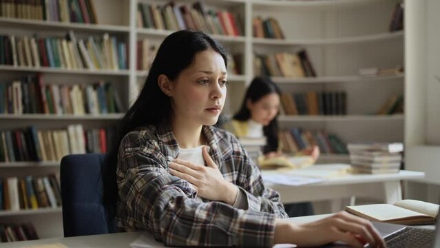Worried young woman student studying at university library while has panic heart attack hold hand on chest and try to calm down indoors Anxious female with mental health problem at classroom