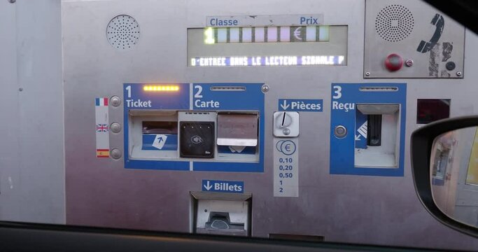 LYON, FRANCE - JUNE 28, 2023: A hand reaches out towards a toll collection machine for a car, interacting with the payment system to settle the toll fee