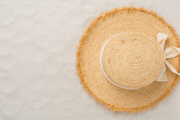 Straw hat on sand background, top view