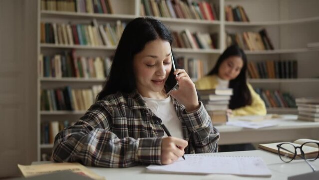 Ill-mannered young student talking on phone very loud at university library and prevents a group mate from preparing for the exam indoors 