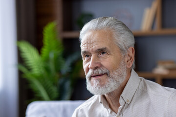 Close-up photo of a smiling gray-haired and bearded senior man at home, thoughtfully and...