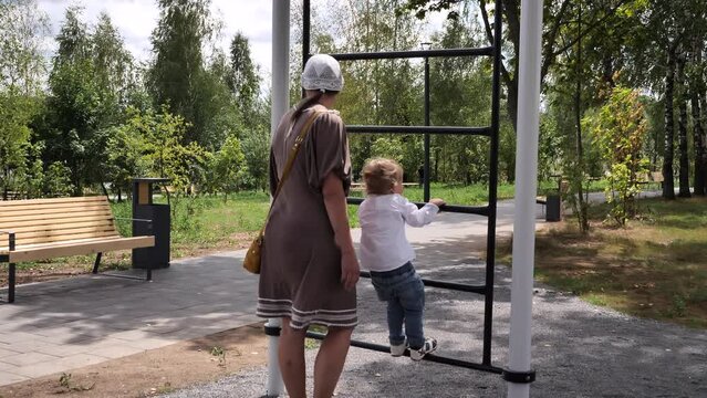 A young mother persuades a small two-year-old toddler not to climb the adult stairs at the playground. Concept: Mother provides a safer playground for the toddler. 