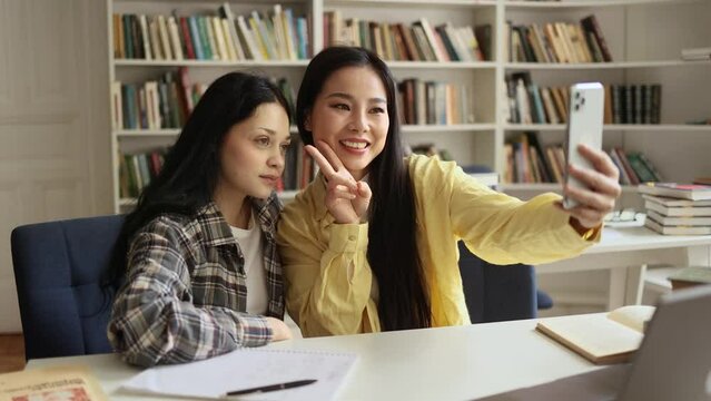 Charming students girls interracial classmates holding smartphone taking selfie photos at university library after lessons at desk Smiling friends enjoying leisure time together indoors