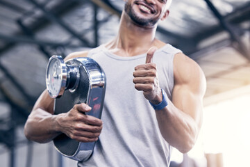 Man, smile and thumbs up with scale in gym for fitness with weight loss or diet with gesture for...