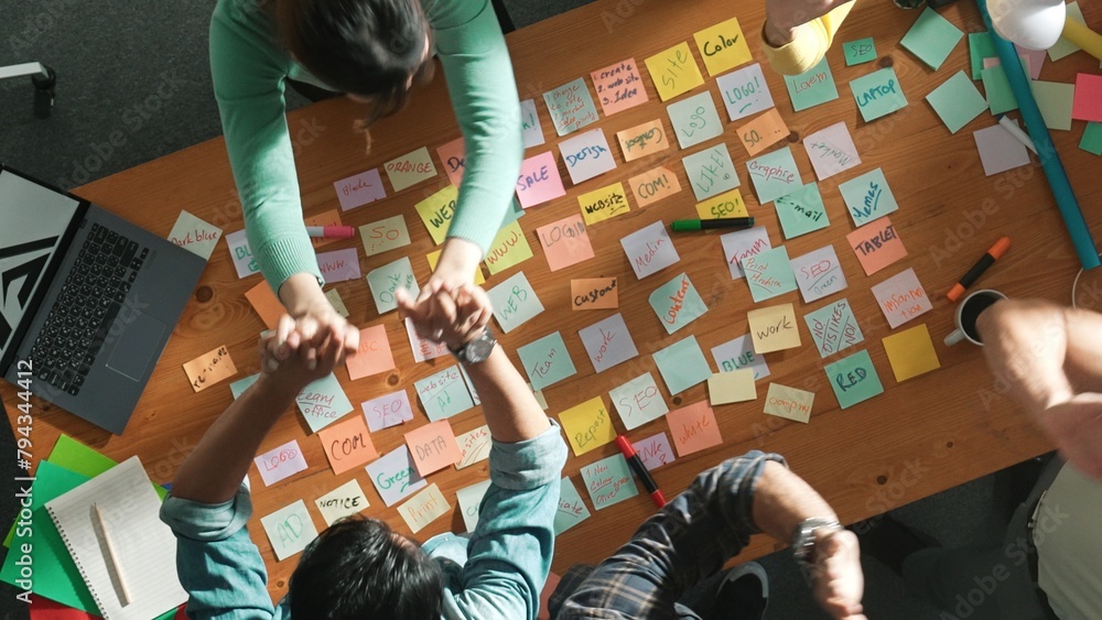 Poster top view of business team giving high five to celebrate project while standing at table with sticky 